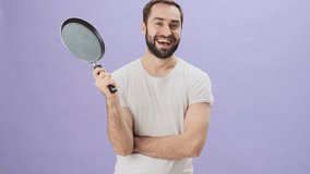 A handsome young man wearing a white t-shirt is holding a frying pan standing isolated over gray background