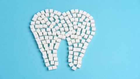 Sugar destroy tooth enamel leads tooth decay White Sugar cubes shape form tooth brown sugar caries Blue background Healthcare and medicine Stomatology concept Sweet food destroy teeth Stop motion