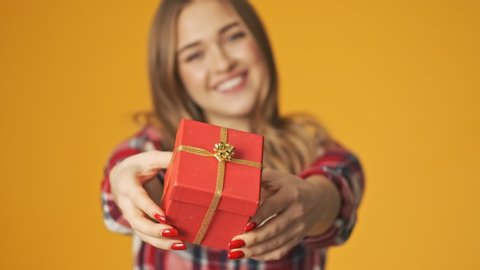 Young happy positive girl isolated over yellow wall background gives you a present box