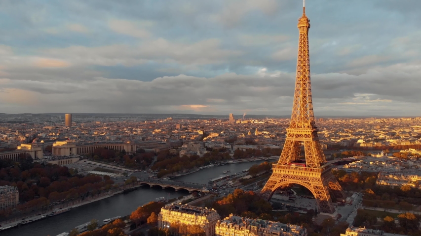 
Aerial drone view of the  Eiffel Tower rising above the Parisian cityscape during golden hour sunset with the Seine River and historic buildings bathed in warm light