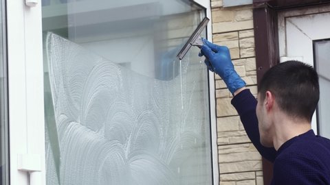 a professional window cleaner soaps and squeegies a window clean, male cleaning worker.