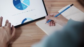 Backview Shot of Businesswoman using digital tablet hand touching on screen scrolling a business financial report on tablet check, analyzing graph and chart while taking notes or report work from home - Powered by Shutterstock - Get 15% off with code: PIKWIZARD15