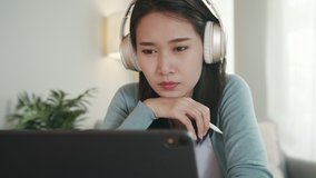 Beautiful Asian Woman Wearing Headphone watching lesson online looking at tablet screen learning online courses, training, online teacher teaching, studying from home. Distance Education Concept.