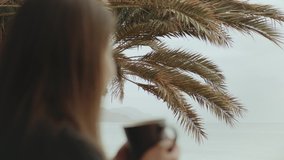 Alone woman is drinking coffee or tea in morning on balcony with blue sea view, point of view from window, rapid video, slow motion, 4k