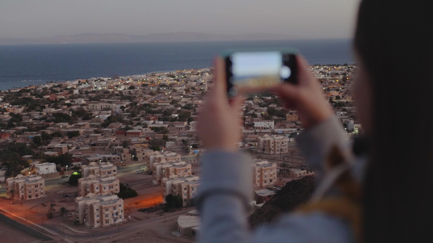 Woman take picture of the sea by smartphone in the evening. Woman stay on top of the mountain and looking Into Horizon, slow motion, 4k