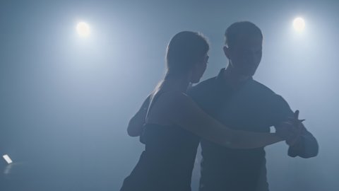 Dance element from tango in slow motion. Graceful latinamerican dance performed by young couple in smoky ballroom. Medium shot in 4K, UHD