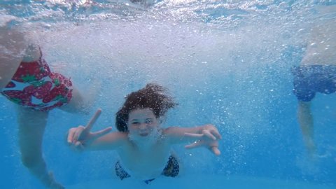 Children enjoying summer vacation. Happy fun loving group of friends jumping and diving into swimming pool at a pool party in summer sunny day. Slow motion. Underwater view