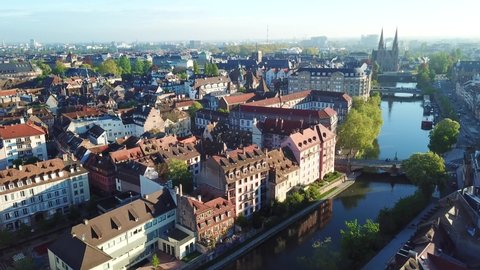 Aerial top view of old historical cityscape. Drone flying over beautiful river, surrounded by amazing old houses and green trees in Petite France. Church on the background. Strasbourg, France 