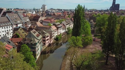 Aerial top view of old historical cityscape. Drone flying over beautiful river, surrounded by amazing old houses and green trees in Petite France. Church on the background. Strasbourg, France 