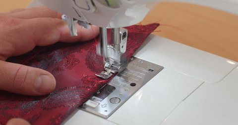 Close-up of Sewing Machine Needle in Motion: the  needle rapidly moves up and down. The tailor sews red paisley lining fabric in the sewing studio workshop. The process of suit making.