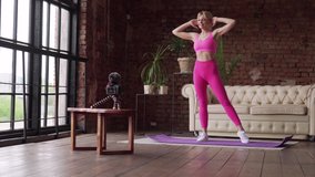 Young woman fitness blogger in sportswear is recording a video as she does exercises at home.