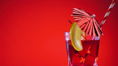 Festive red cocktail in a glass with lemon. Cooling summer drink with umbrella rotate on a red background. Fresh citrus cocktail, healthy drink concept.