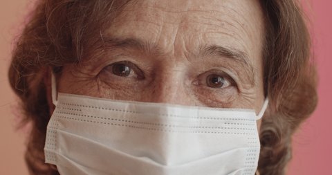 Extreme close up of elderly woman wearing protection mask looking at camera. Eye level, push out, hand-held, single shot, extreme close up, 4K.