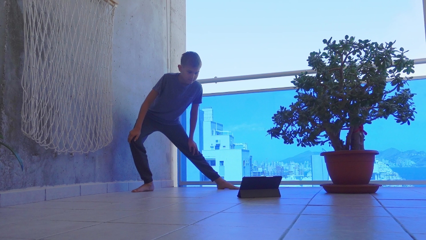 Teenager boy with tablet computer doing sport exercises on balcony. Sport, healhty lifestyle, active leisure at home