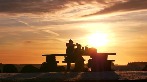 Silhouettes of family picnic,winter sunset with golden cloudscape by the water