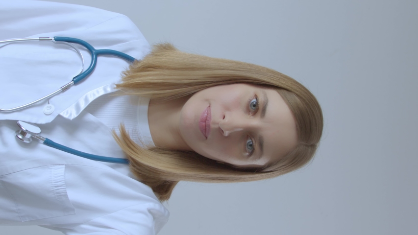 Young smiling female doctor in white uniform with stethoscope talking to camera by conference video call chat. Online consultation in app. Telemedicine, healthcare and e-health concept. Vertical shot | Shutterstock HD Video #1052762771