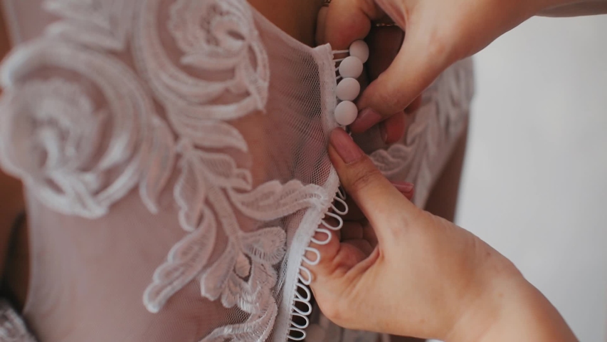 Bride's lace up dress. Bridesmaid tying bow on wedding dress. Woman's hands lace up silk ribbon on bride's corset. Helping to lace up | Shutterstock HD Video #1052764115