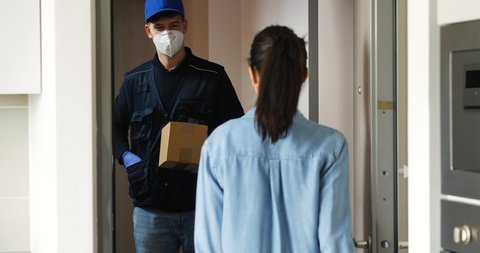 An young woman is receiving a parcel from mailman with a protective mask and gloves delivered in her home. 