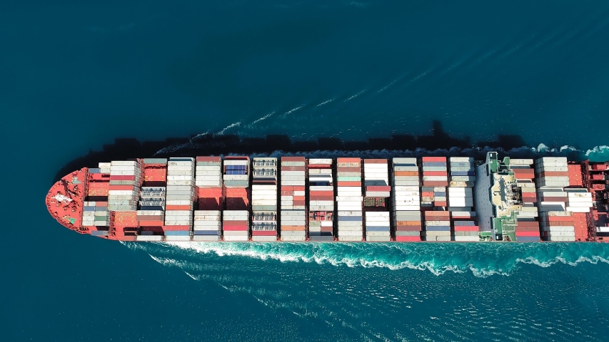 Aerial top down view of a container ship. Her engine roaring at full speed, leaving wake water. Flying over the long cargo ship full of containers sailing in open sea
 | Shutterstock HD Video #1052776178