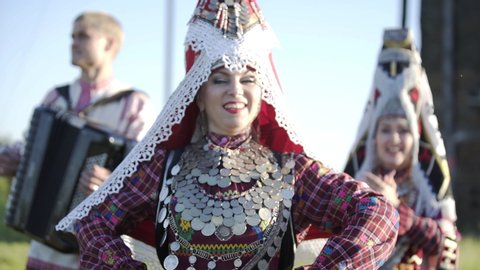 People in traditional russian clothes dancing outdoor on traditional antique wooden windmill background. Group of happy people wearing national Finno-Ugric clothes.