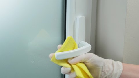 Woman with white rubber gloves spray antibacterial disinfectant and clean office doors handle. Corona virus protection