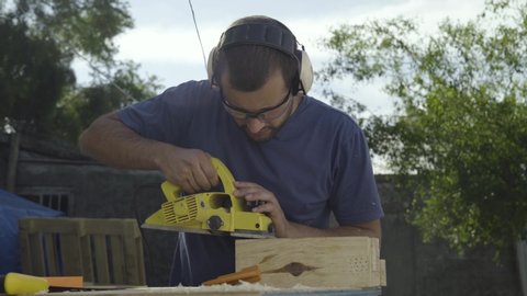 Young male woodworker using power tools to plane and sand lumber