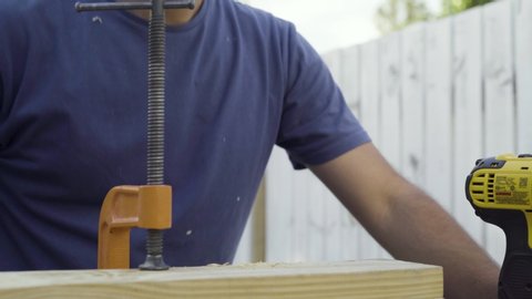 Young male carpenter uses a power tool to drill screws into a plank of wood