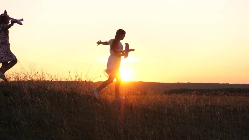 Dreams of flying. Happy childhood concept. Two girls play with a toy plane at sunset. Children on background of sun with an airplane in hand. Silhouette of children playing on plane | Shutterstock HD Video #1052783009