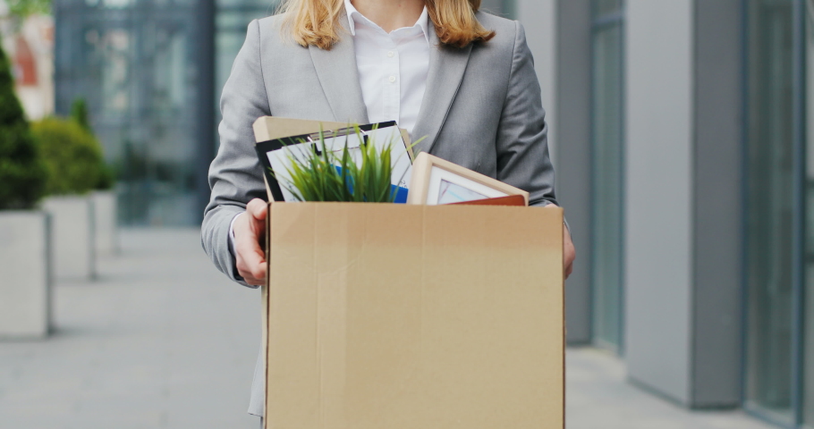 Portrait of Caucasian sad businesswoman in glasses standing outdoors with box of stuff. Leaving business. Female office worker lost her job. Unemployment rate growing. Fired upset desperate woman. | Shutterstock HD Video #1052783384