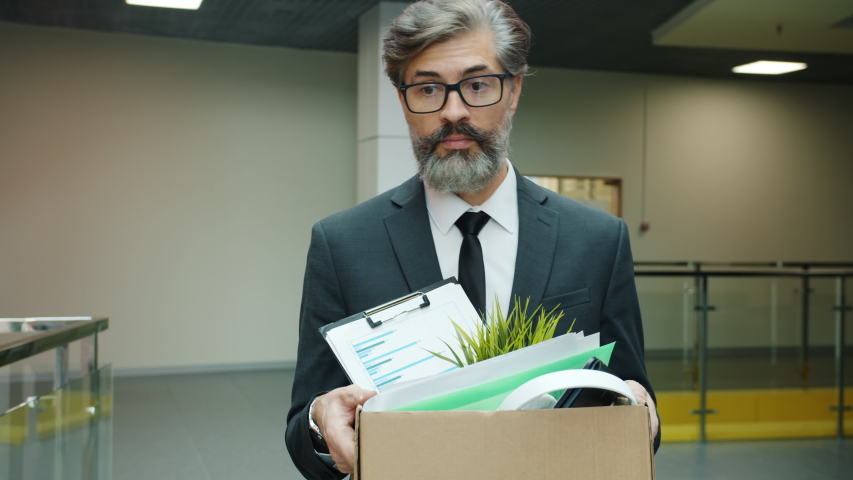Slow motion of depressed fired businessman walking in hall with box of belonging after dismissal feeling unhappy and hopeless. People and work concept. Royalty-Free Stock Footage #1052785022