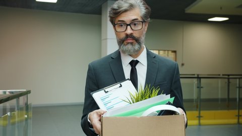 Slow motion of depressed fired businessman walking in hall with box of belonging after dismissal feeling unhappy and hopeless. People and work concept.
