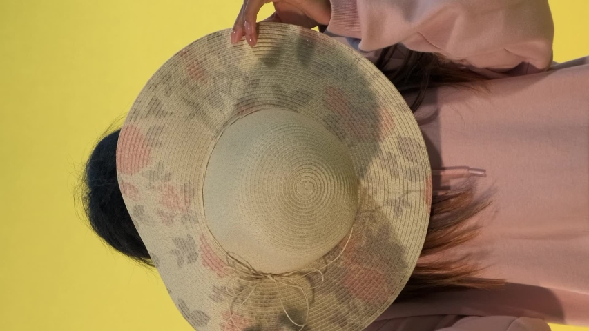 Smiling african woman hiding behind the hat on yellow background. She playing with someone. Video with Vertical Screen Orientation 9:16