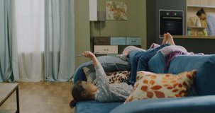 Pre-school Caucasian girl lying on a sofa, playing games or wathcing cartoons on a tablet. Parents cooking in the background. Shot on RED Helium