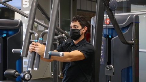 Cape Town, South Africa - May 2020: Attractive Man in Gym doing Shoulder Press on machine Wearing Protective Mask, Covid 19, Corona Virus Pandemic in Africa, alone social distancing. close up shot.