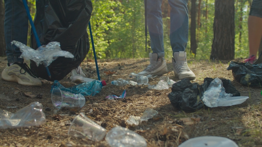 Low section of diverse young volunteers tidying up rubbish in forest using garden tools. Group of charity eco activists picking up plastic waste and garbage in woodland. Environmental awareness.