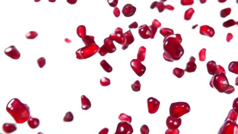 Shiny grains of ripe pomegranate are flying diagonally on a white background in slow motion, loop footage