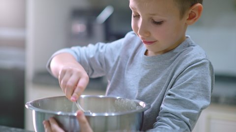 Slow motion 4k footage - Boy cooking at the kitchen. White boy stirring dough for a cookie. Kid is mixing ingredients for a cake in the steel bowl. 8 years old child cooking food at home. 