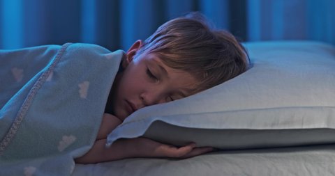 4k footage  of a sleeping child in bed.  8 years old boy sweetly sleeping in his crib. Face close-up of a sleeping child on its side. Tracking shot of a sleeping kid at midnight. Relax and resting