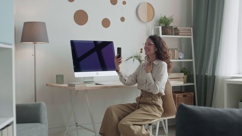 Pan shot of Caucasian woman with curly hair sitting on chair at home, looking at mobile phone Stock Video