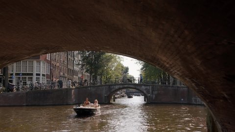 Amsterdam, Netherlands - 01-07-2019: Beautiful shot of bridge over canal in Amsterdam. People enjoying summer in a boat. Amsterdam is the capital and most populous city in Netherlands. 