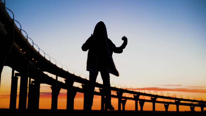 Silhouette of man dancing at sunset at the bridge to the lake