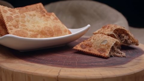 Fried pastry on a plate and a meat pastry cut in half on the wooden board