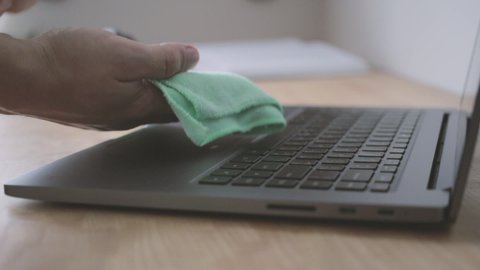 Male hand cleaning and sanitizing keyboard of laptop from dust and viruses, coronavirus protection and disinfection