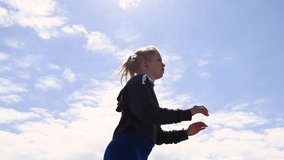 Attractive young Scandinavian, Caucasian woman, jumping up and down as exercise, in real time. The camera is looking up at her. It’s a beautiful sunny day with blue sky and some clouds. Stock footage 
