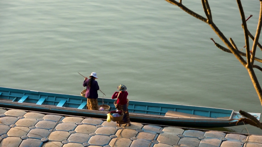 Two local ladies loading their long boat on the MeKong river in Vietnam. Slow flow on Mekong river on the background. Traditional old wooden boat used to cross river. Local transportation method