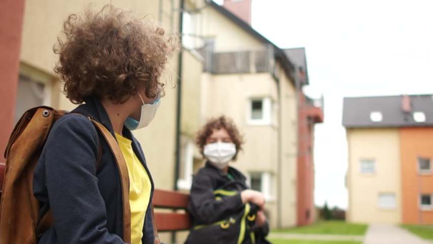 Children in protective masks with satchels behind their back stand up from the bench and say goodbye to their elbows