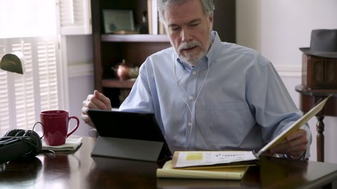 A team leader in his living room holding a video meeting via his tablet pc with team members collaborating virtually due to the pandemic and the new reality in 2020 of working from home.