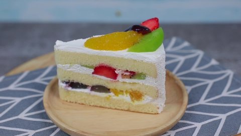 Slice of layered creamy fruit cake. Fruit layer cake , Slice of the layered sponge cake with milk cream coating and decoration with slices of fresh fruits and berry on a wooden plate rotating