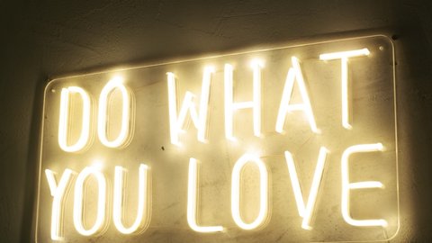 title that says do what you love made of yellow neon light on wall. festive decoration of interior. illuminated letters of elecrical tubes shine bright in the evening. motivation quote, symbolic sign