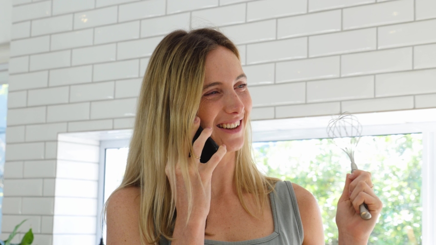 Beautiful female talking on the phone while baking in the kitchen